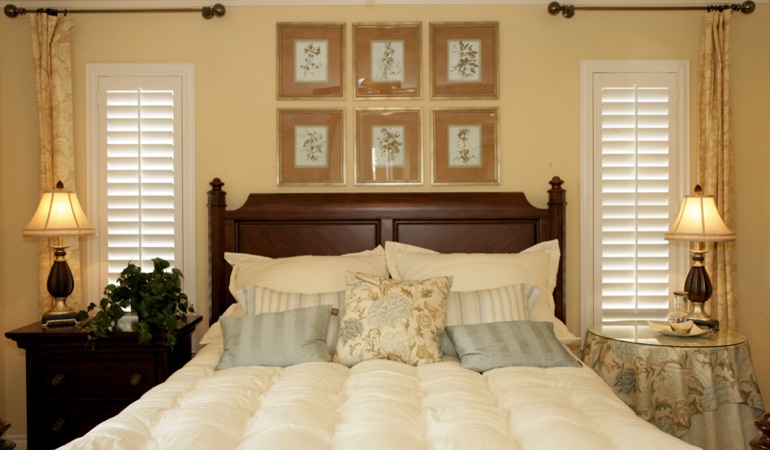 Tall plantation shutters framing bed in a bedroom in Hartford 